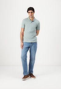 Lys grøn polo skjorte med korte ærmer, parret med blå jeans og brune sneakers. Enkel design, afslappet pasform, og glat tekstur.