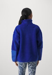 Fleecepolo i klarblått, med hög krage, oversized passform och kontrasterande blå ärmar; textil med en mjuk finish.