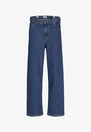Dziecko w zielonym morskim t-shircie z napisem "JACK & JONES", luźnych ciemnoniebieskich dżinsach i białych trampkach, stojące z rękami w kieszeniach.