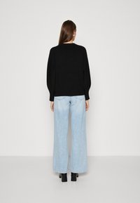 Suéter negro con mangas abullonadas, combinado con jeans de pierna ancha en azul claro y botas negras de tacón cuadrado. Diseño sencillo, sin patrones notables.