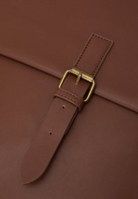 Fermeture de sac en cuir brun avec une surface texturée, une boucle en laiton et une sangle assortie avec plusieurs trous d'ajustement.