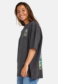 T-shirt oversize grigia in cotone, con una stampa grafica quadrata sul petto sinistro e un design più grande sul retro con motivi colorati.