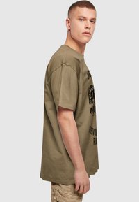 Khaki bomulls t-skjorte med løs passform, korte ermer og grafisk tekstdesign på fronten. Glatt tekstur og rund halsutringning.