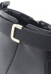 Lasbotas negras hasta el tobillo presentan un cuerpo de cuero liso con una banda texturizada negra y herrajes dorados. El diseño incluye una cremallera lateral para el cierre.