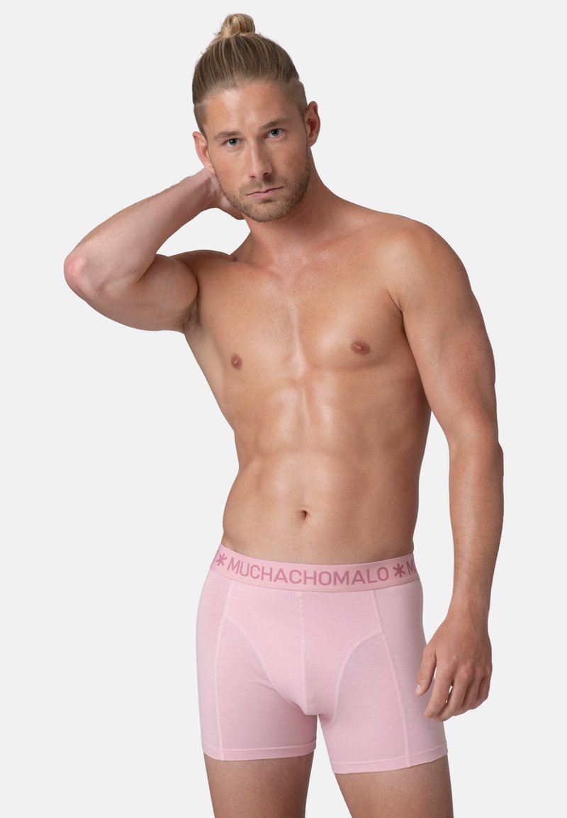 Svetlo roza bokserice s blagovno znamko na pasu. Tkanina se zdi mehka in gladka, z oprijetim fitom in ravnimi šivi.