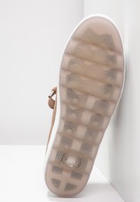 Semelle de chaussure avec une semelle en caoutchouc transparente et texturée et un coussin d'air circulaire près du talon, montrant le motif de la bande de roulement et une partie de la tige marron clair.