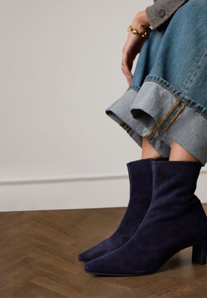 Marineblauwe suède enkellaarsjes met een taps toelopende neus en blokhak, gecombineerd met een denim rok met een rafelige zoom en contrasterende stiksels.