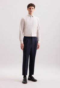 Jasny beżowy koszula z subtelnym wzorem w paski, w połączeniu z granatowymi spodniami z wysokim stanem i czarnymi skórzanymi butami.