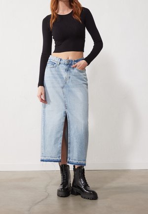 Falda de mezclilla azul clara con una abertura en la parte delantera, combinada con un crop top negro de manga larga acanalada y botas negras de suela gruesa con cordones.