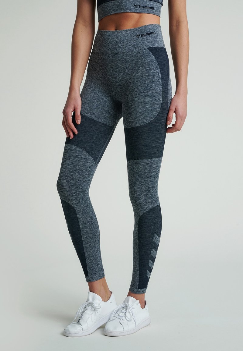 Grå atletiska leggings med kontrasterande marinblå patchar, hög midja och strukturerad tyg. Funktioner logotyp och geometriska accenter på sidan.