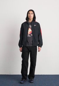 Chaqueta bomber negra con acentos rojos, camiseta gráfica gris con un balón de baloncesto, pantalones negros y zapatillas deportivas negras. Textura plana, estilo casual.