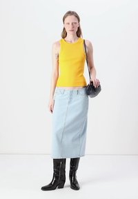 Žuta rebrasta majica na bretelama, svijetloplavi jeans midi suknja, crne lakirane čizme do koljena i mala crna torbica.