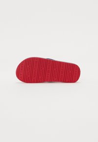 Rød gummisåle med preget "TOMMY HILFIGER" tekst og horisontale linjer. Har en avrundet tå og konturert design for komfort.