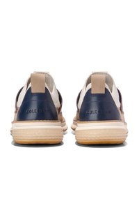 Zadní pohled na tenisky s námořnickou koženou patou, béžovým textilním svrškem a světlou gumovou podrážkou s texturovaným gripem. Na patě je embosováno "Cole Haan".