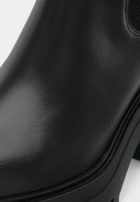 Čierne kožené členkové topánky s hladkým, lesklým povrchom, ktoré majú robustnú podrážku a elastický bočný panel. Minimalistický dizajn s čistými líniami.