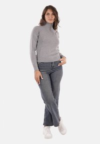 Maglione grigio aderente a collo alto con maniche lunghe, abbinato a jeans in denim scuro a gamba dritta con vita alta e sneakers bianche.
