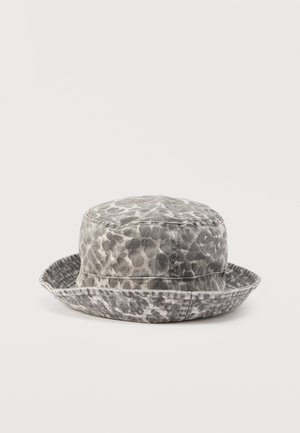 Hall ja valge leopardimustriga kaabuga müts, millel on pehme õmmeldud serv, lebab valgel tasasel pinnal.