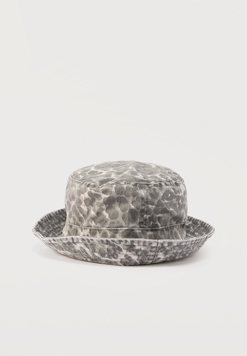 Chapeau seau à imprimé léopard gris et blanc avec une bordure douce cousue, posé sur une surface blanche unie.