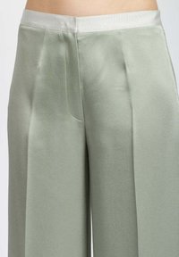 Pantaloni larghi di colore verde chiaro realizzati in tessuto morbido, con una vita elasticizzata e tasche laterali, che mostrano un taglio pulito e sartoriale.
