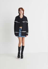 Cămașă tie-dye alb-negru cu două buzunare în față, purtată peste un top scurt negru, asortată cu o fustă mini din denim și cizme negre până la genunchi.