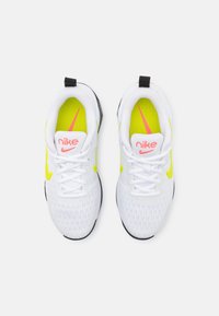 Zapatillas deportivas blancas con detalles de malla, acentos en amarillo neón, logo de Nike en rosa y suela negra. Cuentan con cordones y cuello acolchado.