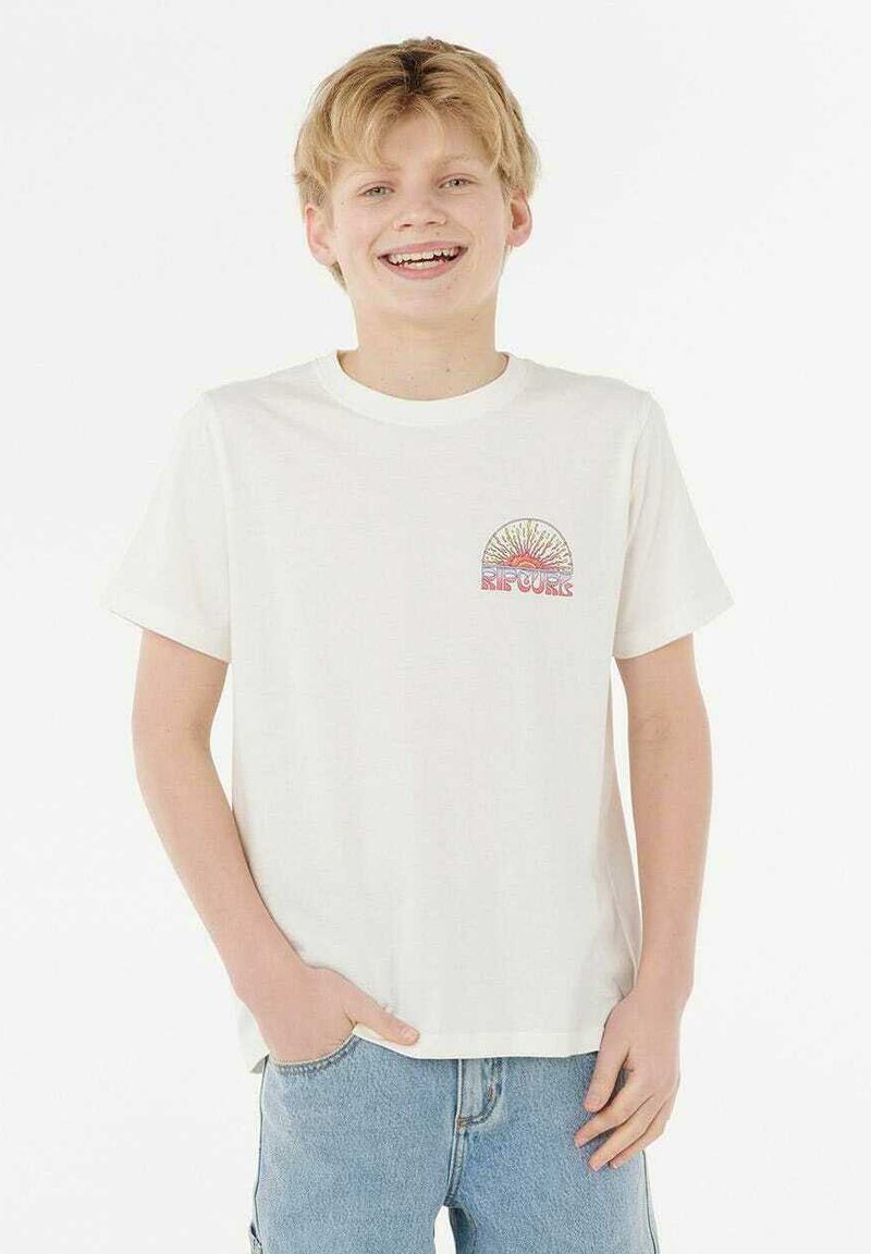 Camiseta blanca de algodón con mangas cortas, que presenta un gráfico multicolor circular en la parte izquierda del pecho. Se lleva con jeans de mezclilla azul claro.