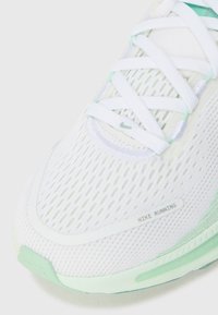 Chaussure de course blanche avec un dessus en mesh, des accents vert menthe et des détails réfléchissants. Présente des lacets blancs plats et une semelle texturée.