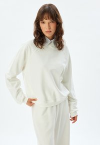 Sudadera blanca de corte holgado con puños acanalados, combinada con una camisa de rayas con cuello. Textura suave y detalles de diseño mínimos.
