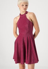 Εφαρμοστό φόρεμα με λαιμόκοψη halter από υφασμάτινη διχρωμία σε σκούρο ροζ, φαρδύ σχέδιο φούστας με τσέπες στα πλάγια, ελάχιστη γυαλάδα και επίπεδες ραφές.