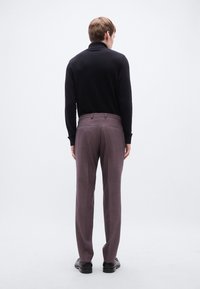 Μαύρο πουκάμισο με μακριά μανίκια και απαλή υφή, συνδυασμένο με ανοιχτό μοβ παντελόνι με καρό σχέδιο, φορεμένο με μαύρα παπούτσια, από πίσω.