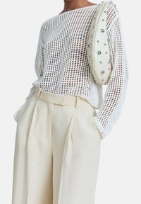 Pull en maille blanche avec un large col, associé à un pantalon crème taille haute. Le sac présente une texture lisse avec des accents en argent.