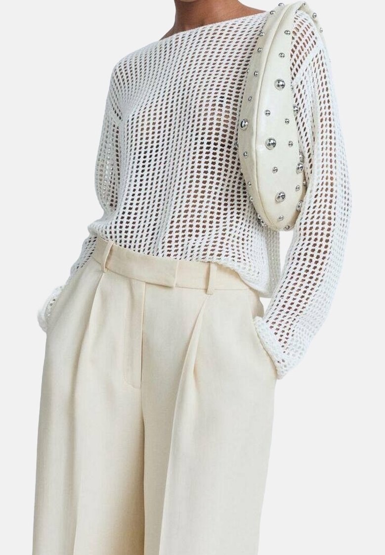 Pull en maille blanche avec un large col, associé à un pantalon crème taille haute. Le sac présente une texture lisse avec des accents en argent.