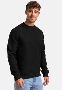 Felpa nera a girocollo con motivo testurizzato, maniche lunghe e polsini a costine. Abbinata a jeans blu chiaro, che mostrano un look casual.