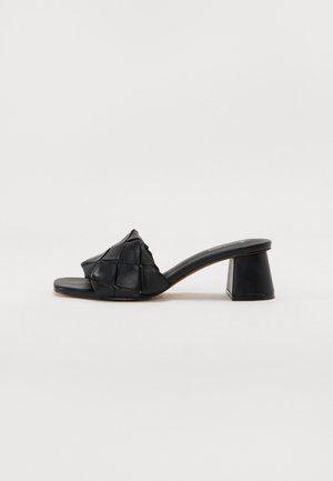 Sort mule sandal med åben tå, flet overdel i læder og blokhæl på hvid baggrund.