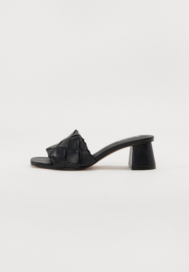 Mule noire à bout ouvert avec dessus en cuir tressé et talon bloc sur fond blanc.