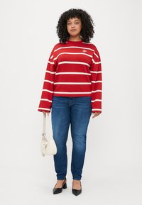 Sweatshirt rayé rouge avec des manches longues et un col rond, associé à un jean bleu, des talons noirs et un petit sac à main blanc.