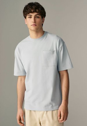 Jasnoniebieski t-shirt z krótkim rękawem, wykonany z bawełny, z małą kieszonką z przodu oraz luźnym krojem. Gładka struktura z okrągłym dekoltem.