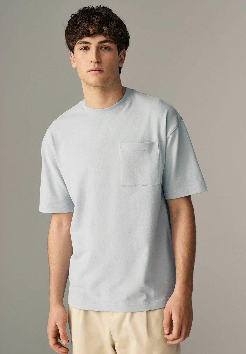 Lyseblå kortærmet t-shirt lavet af bomuld, med en lille frontlomme og en afslappet pasform. Glat tekstur med rund hals.