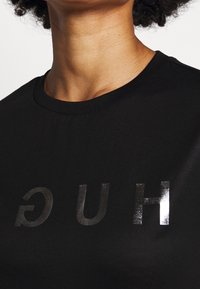 Camiseta negra de algodón, que presenta una impresión plateada brillante de la palabra "HUG" mostrada al revés en el frente.