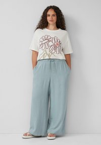 T-shirt blanche avec un design graphique floral, associée à un pantalon bleu clair à coupe décontractée. Les pantalons ont des poches latérales et une taille à cordon.