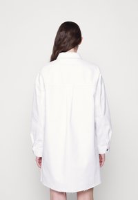 Vestido branco oversized com botões, de mangas longas, com colarinho e bainha desfiada. Feito de um tecido texturizado, com um corte descontraído.