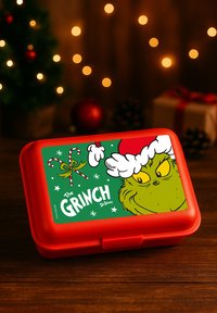 Red lunchbox featuring a cartoon Grinch with a white hat, surrounded by candy canes and snowflakes on a green background.