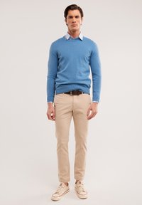 Pullover azzurro chiaro, maniche lunghe, sopra una camicia collare azzurro chiaro. Chinos beige e sneakers chiare con accenti rossi. Aspetto casual ordinato.