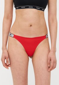 Rode katoenen stringonderbroek met een zwarte elastische tailleband met het "HUGO" logo. Eenvoudig, minimalistisch ontwerp met een gladde textuur.