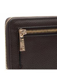 Brązowy skórzany portfel o fakturowanej powierzchni, z zamknięciem na złoty zamek błyskawiczny i małą metką z logo na suwaku.