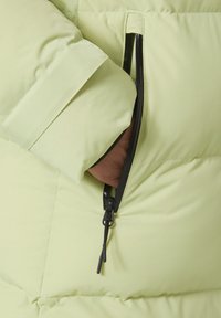 Giacca puffer verde chiaro con una texture morbida, dotata di una tasca con zip e dettagli neri per contrasto.