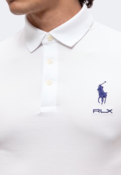 Homme portant un polo blanc à col avec trois boutons et un logo bleu brodé représentant un joueur de polo à cheval avec le texte RLX.