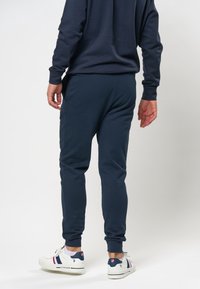 Mörkblå joggers i bomullsblandning med smal passform och elastiska muddar. Kombination med vita sneakers med marinblå och röda accenter.