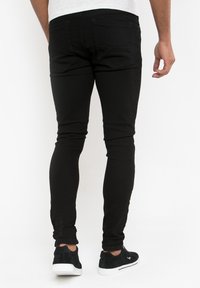 Černé úzké džíny z denimu s hladkou texturou. Mají standardní zadní kapsy a zúžené nohavice, spárované s černými teniskami.