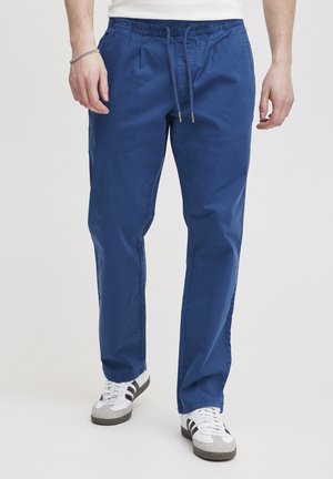 Blue cotton trousers with an elastic waistband and drawstring, featuring side pockets and a straight-leg design. Worn with white sneakers.